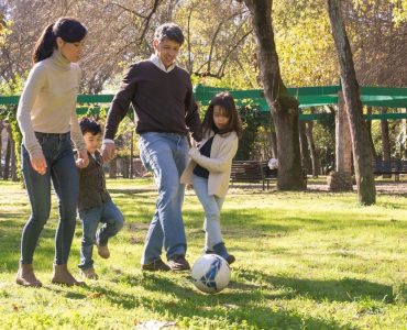A family plays soccer together in a sunny park, enjoying quality time outdoors.