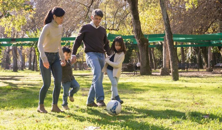 A family plays soccer together in a sunny park, enjoying quality time outdoors.