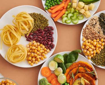 A vibrant mix of legumes, vegetables, nuts, and pasta arranged on white plates showcasing a balanced, healthy diet.