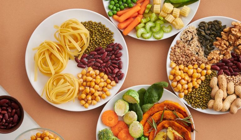 A vibrant mix of legumes, vegetables, nuts, and pasta arranged on white plates showcasing a balanced, healthy diet.